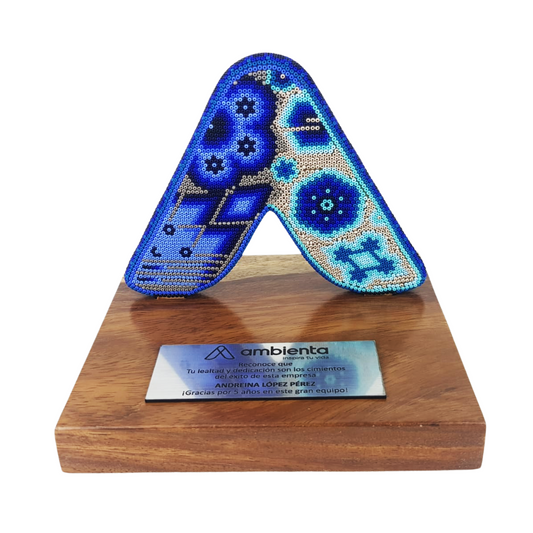 Reconocimiento con artesanía mexicana. Letra A con arte wixárika en trofeo con base de madera y placa metálica personalizada
