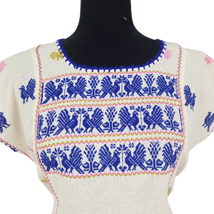 Blusa grande de corte recto con bordados de hilván tradicionales de Puebla, en color blanco con detalles en pecho, mangas y parte inferior. Hecha por Hilaria Gómez.