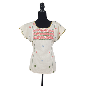 Blusa grande de corte recto con bordados de hilván tradicionales de Puebla, en color blanco con detalles en pecho, mangas y parte inferior. Hecha por Hilaria Gómez.