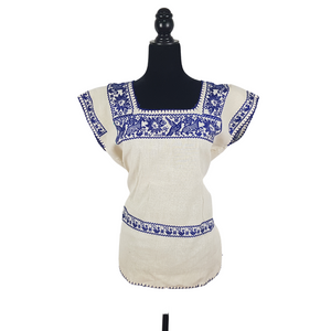 Blusa grande de corte recto con bordados de hilván tradicionales de Puebla, en color blanco con detalles en pecho, mangas y parte inferior. Hecha por Hilaria Gómez.