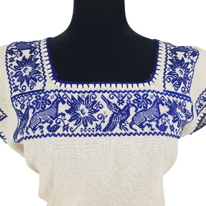 Blusa grande de corte recto con bordados de hilván tradicionales de Puebla, en color blanco con detalles en pecho, mangas y parte inferior. Hecha por Hilaria Gómez.