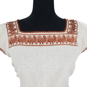 Blusa grande de corte recto con bordados de hilván tradicionales de Puebla, en color blanco con detalles en pecho, mangas y parte inferior. Hecha por Hilaria Gómez.