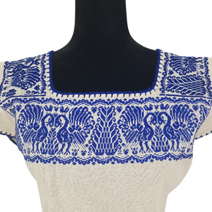 Blusa grande de corte recto con bordados de hilván tradicionales de Puebla, en color blanco con detalles en pecho, mangas y parte inferior. Hecha por Hilaria Gómez.